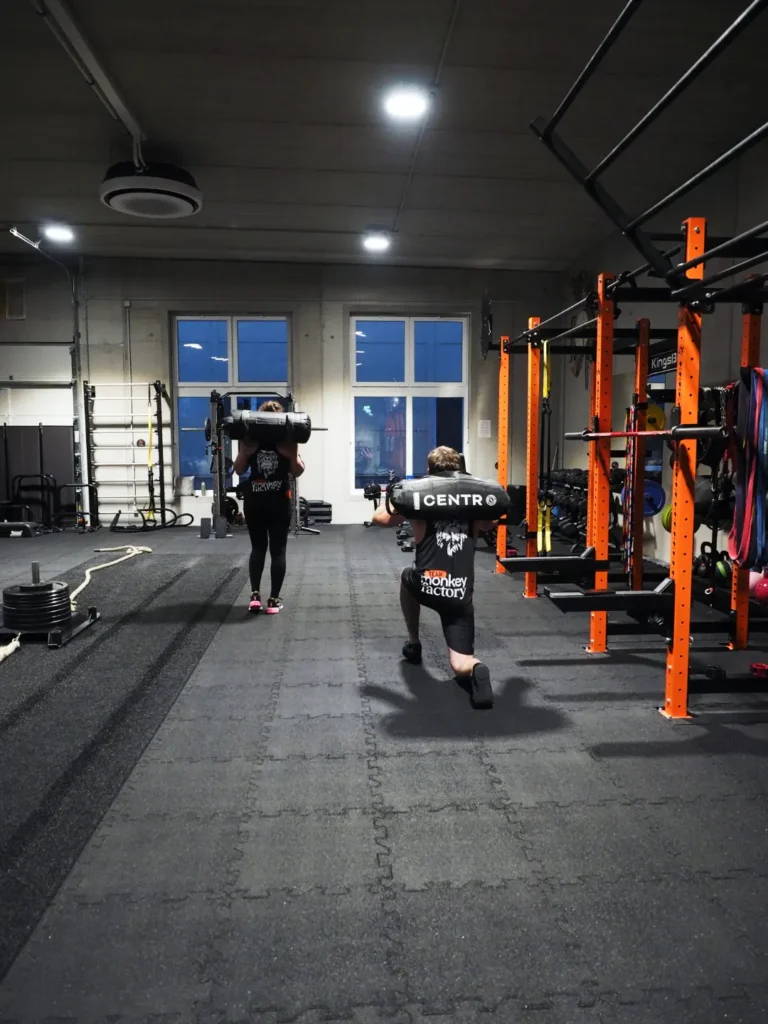 Zwei Personen trainieren Sandbag Lunges